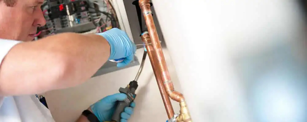 Water heater repair technician testing copper pipe connections and controls in Colorado Springs, CO